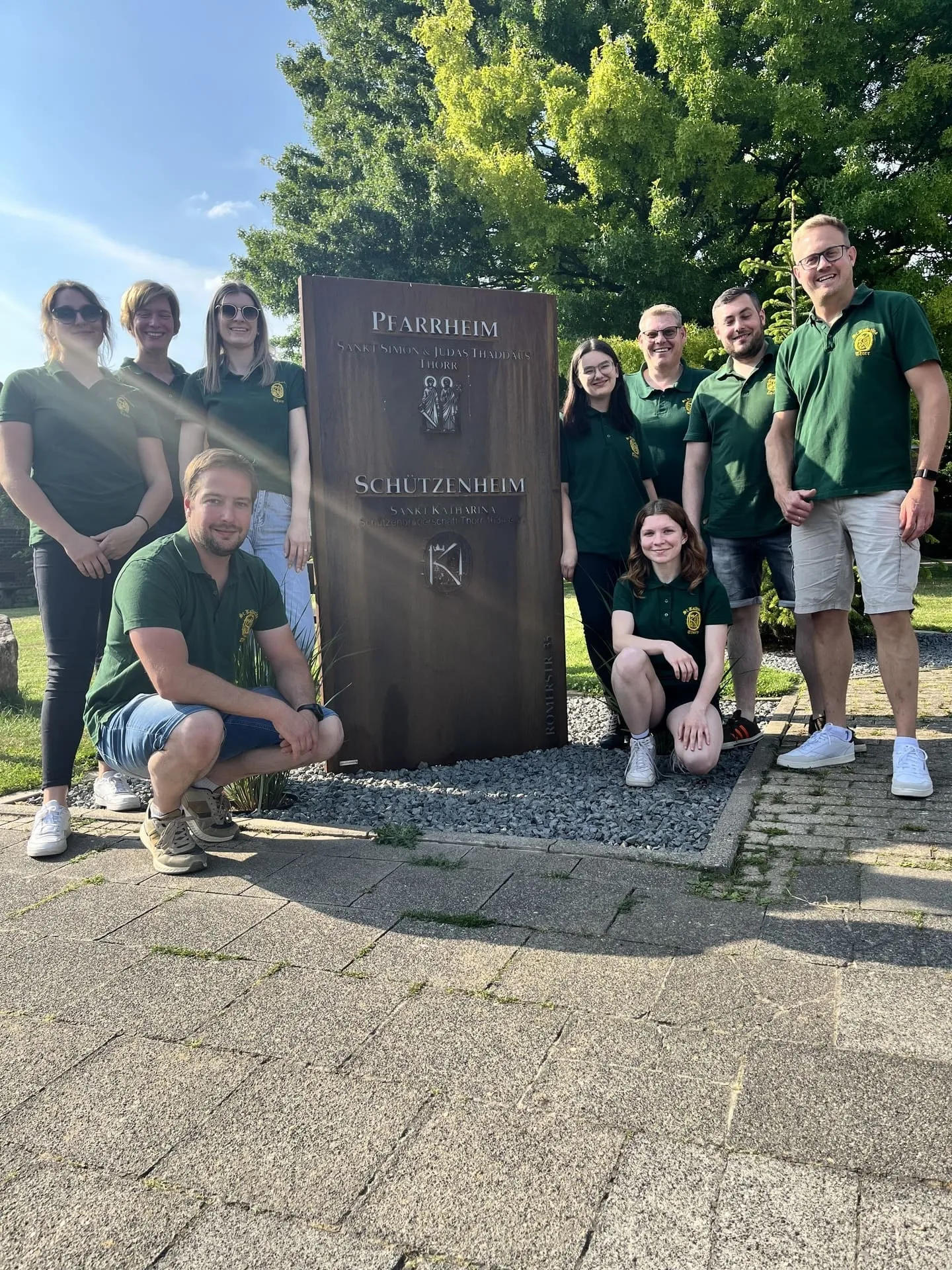 Gruppenfoto der Bruderschaft vor der Cortenstahl-Stele „Pfarrheim / Schützenheim"