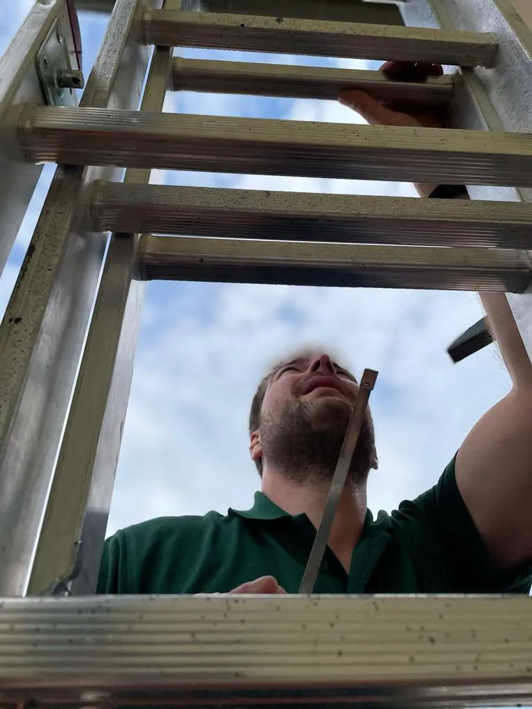 Untersicht – Schützenbruder steigt mit Hammer eine Aluleiter hoch, blauer Himmel im Hintergrund