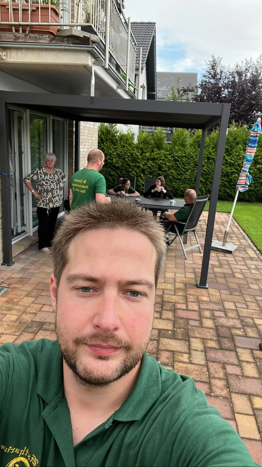 Selfie eines Schützenbruders auf einer Terrasse, Helfer machen Pause unter dem Pavillon im Hintergrund
