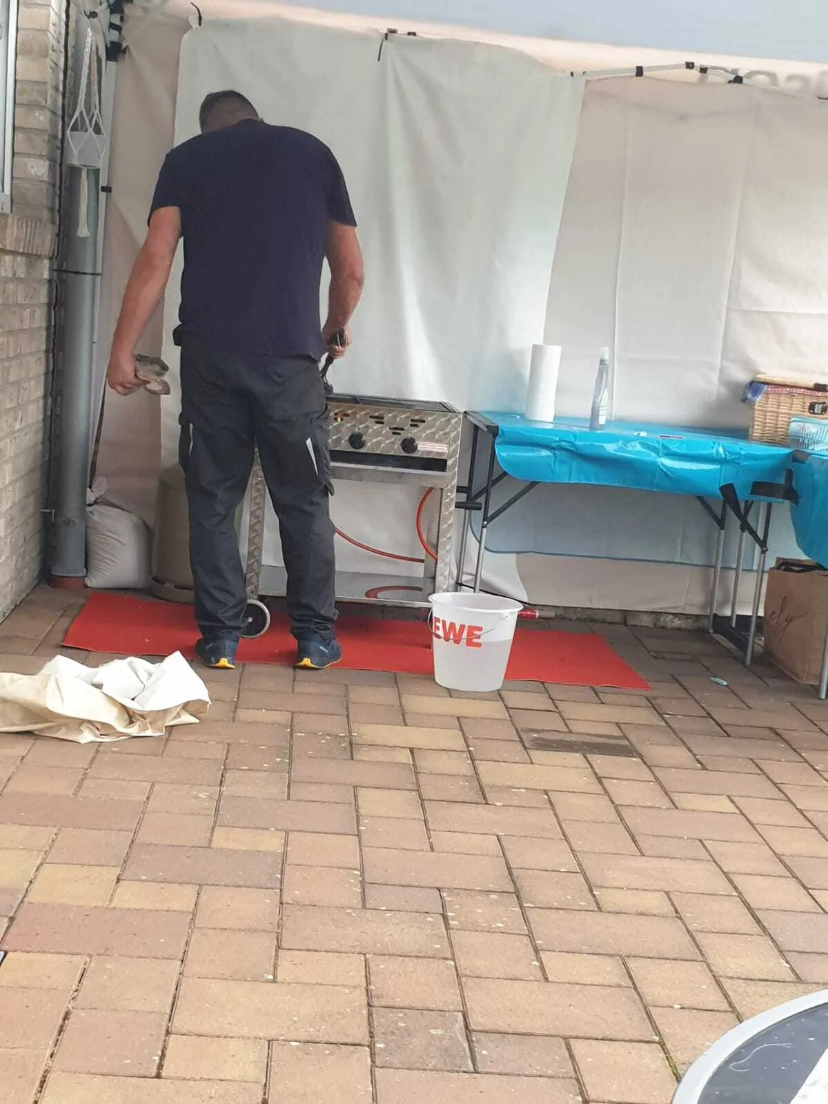 Helfer am Gas-Heißluftgerät beim Vorbereiten des Pavillons, daneben ein REWE-Eimer mit Wasser