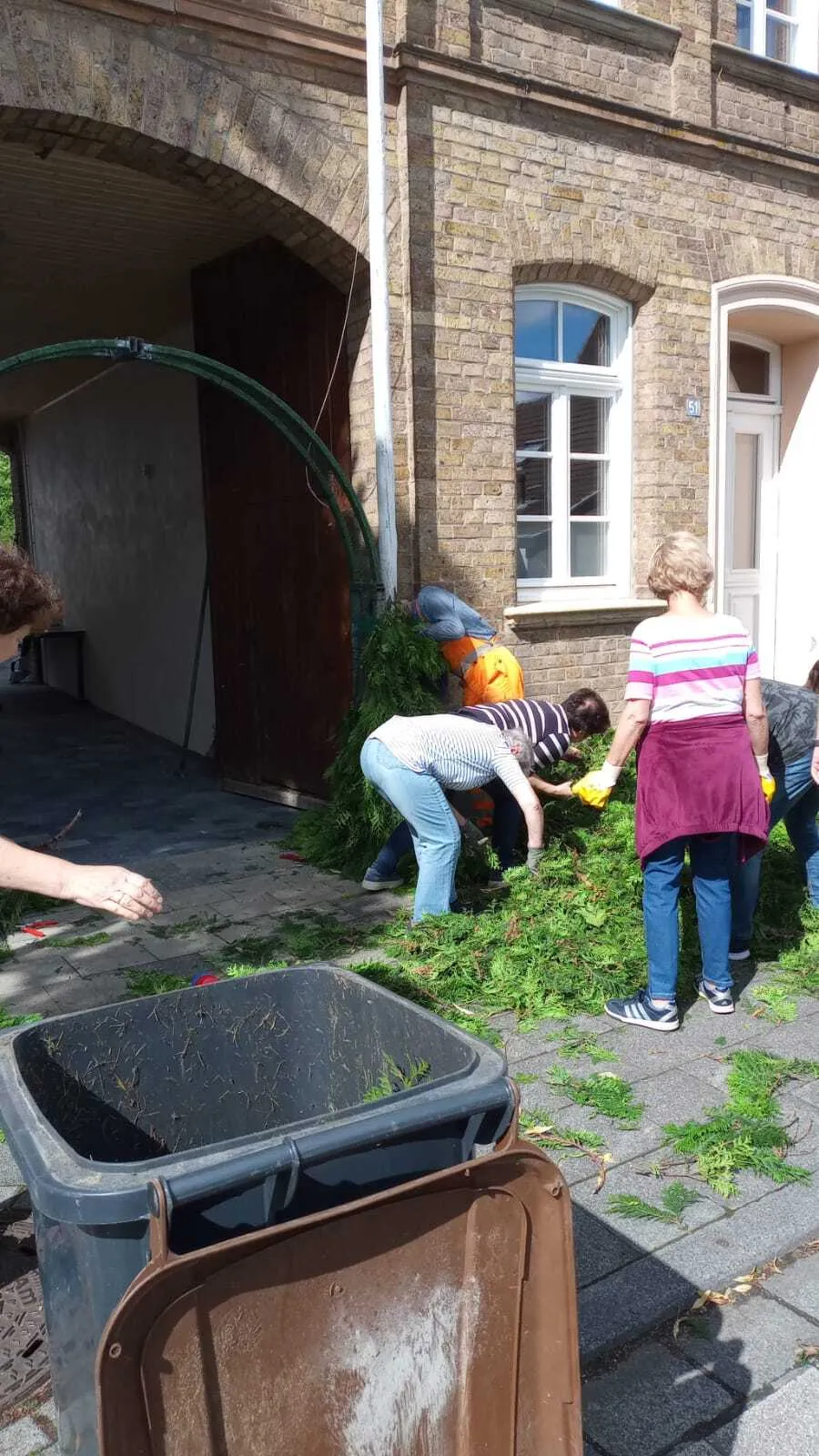Helferinnen und Helfer biegen sich vor dem grünen Tor-Bogen, um Tannenzweige einzustecken