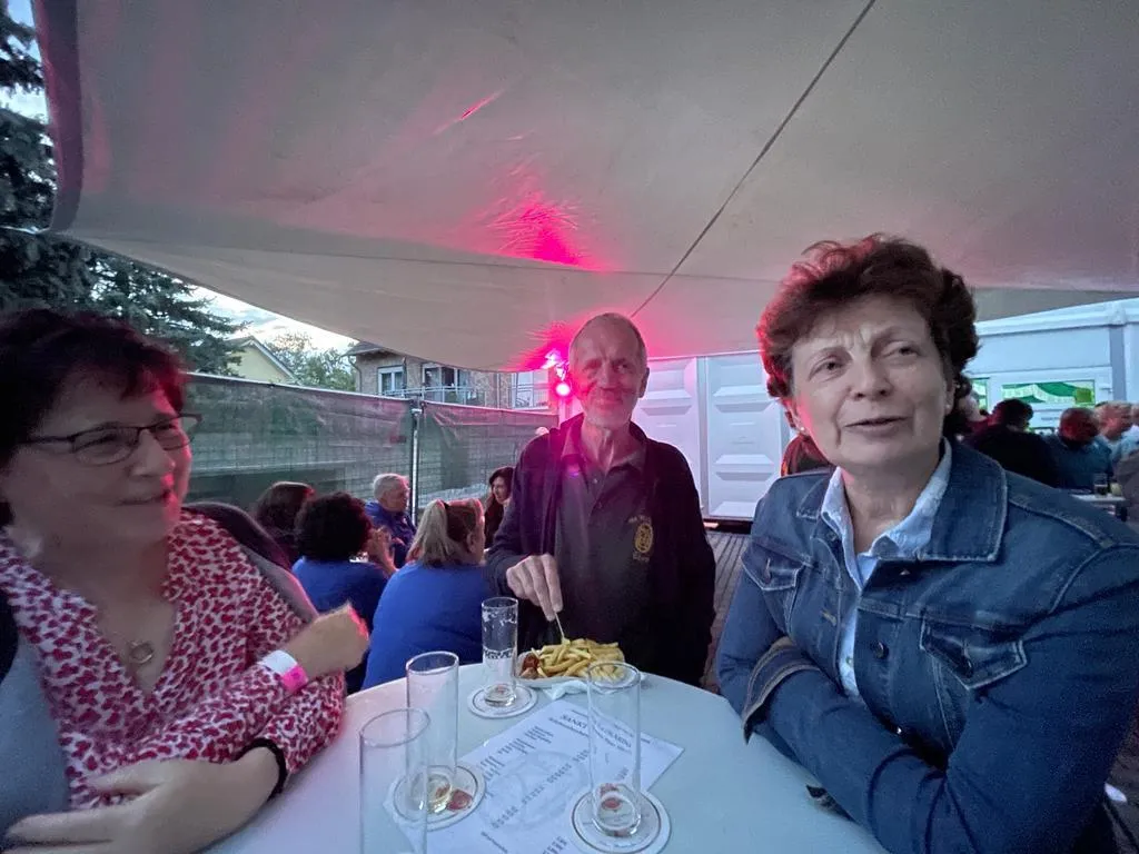 Drei Vereinsmitglieder am Tisch der Sommernacht 2023 mit Pommes und Getränken in rot beleuchtetem Festzelt
