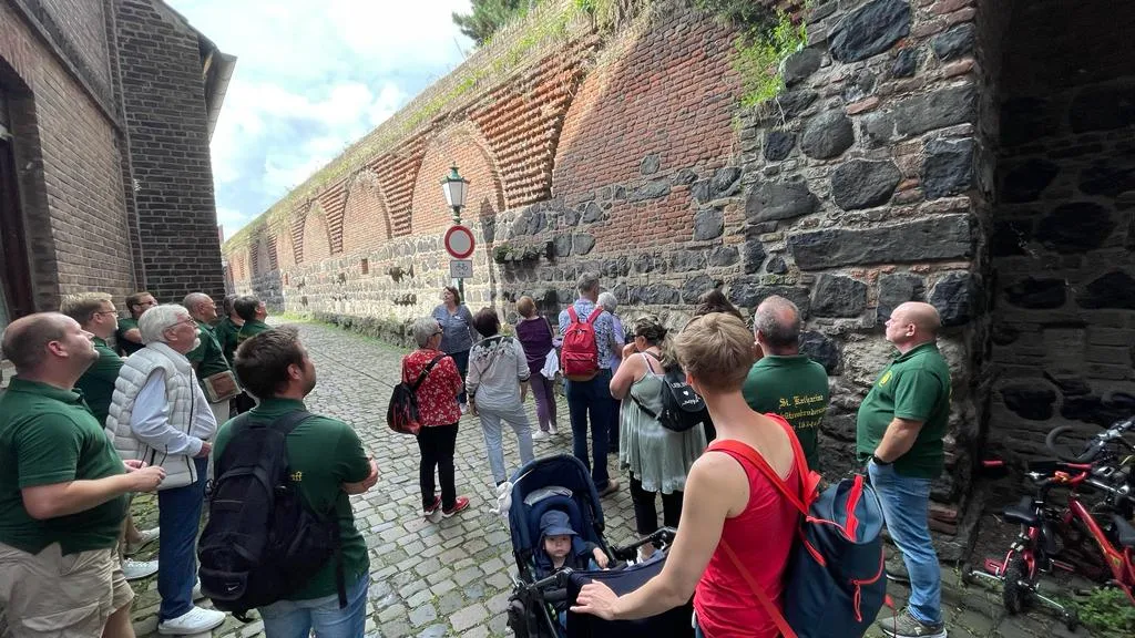 Bruderschaft schaut auf die historische Stadtmauer mit Bogenfenstern und Rheinturm-Mauerring