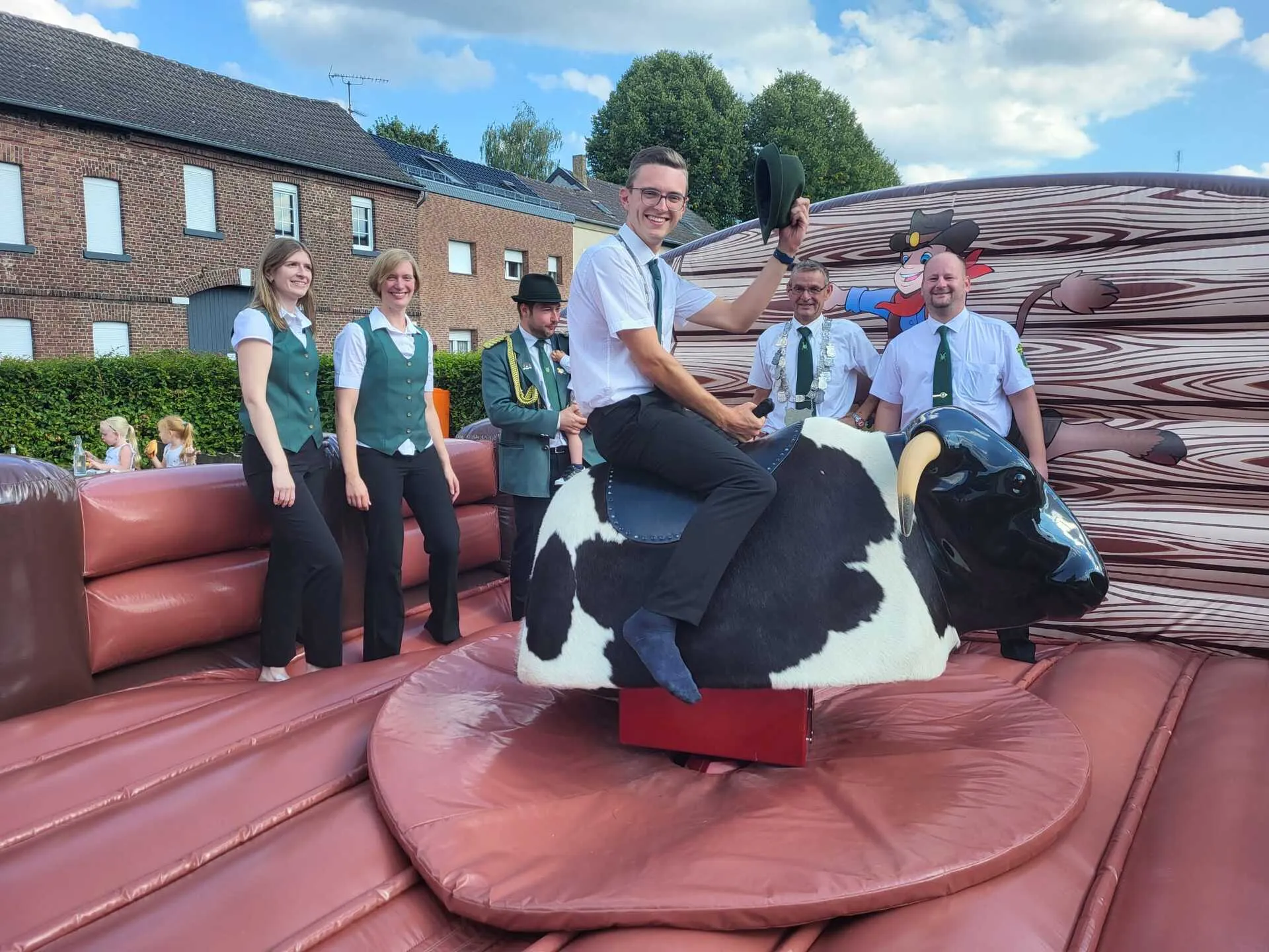Schützenkönig reitet auf dem Bullriding-Bullen, Vereinsmitglieder schauen zu