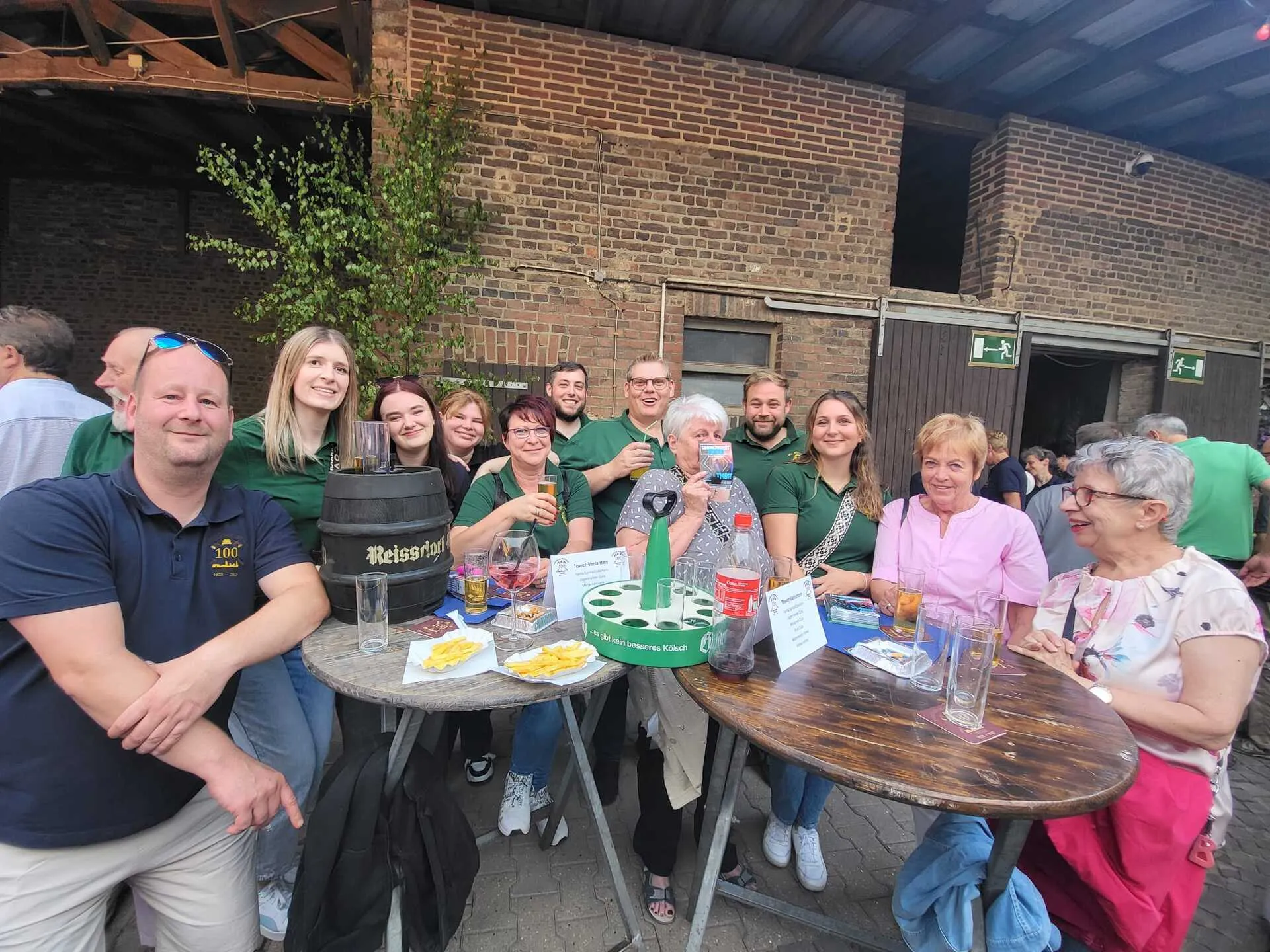 Gruppe der Bruderschaft Thorr mit Reissdorf-Bierfass und Pommes-Tellern an Stehtischen vor einer Backstein-Scheune beim Jubiläumsfest