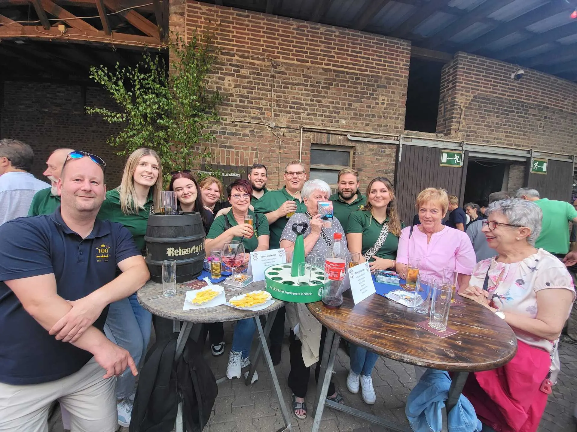 Gruppe der Bruderschaft Thorr mit Reissdorf-Bierfass und Pommes-Tellern an Stehtischen vor einer Backstein-Scheune beim Jubiläumsfest