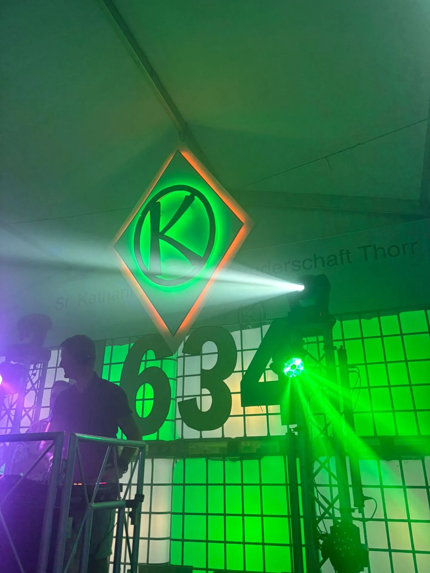 DJ am Pult vor dem grün leuchtenden K-Wappen und dem „634"-Schriftzug, grüner Lichtstrahl im Nebel